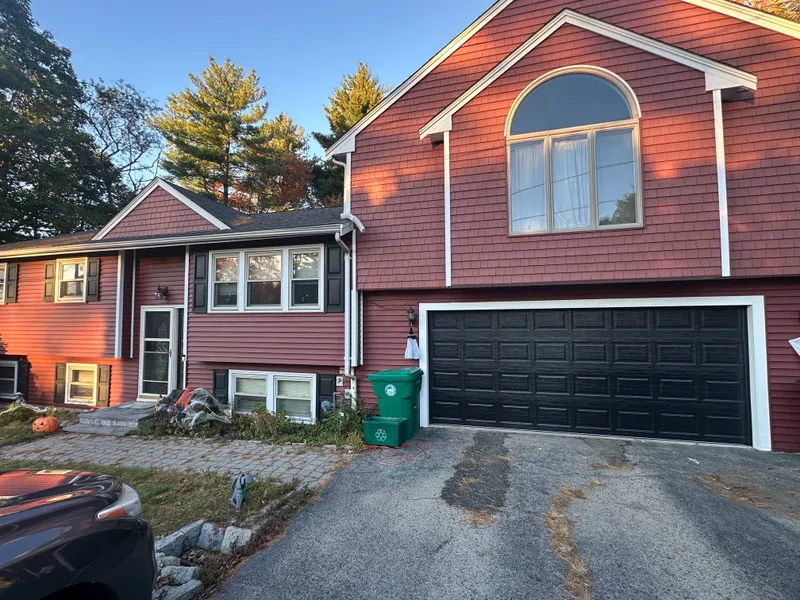 Black raised-panel double garage door on red-sided home with arched window